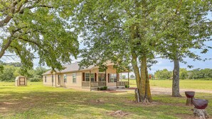 A single-story house with a porch, surrounded by a grassy yard and trees. - 3 Mi to Arkansas River: Rural Family Home w/ Yard (Spiro)