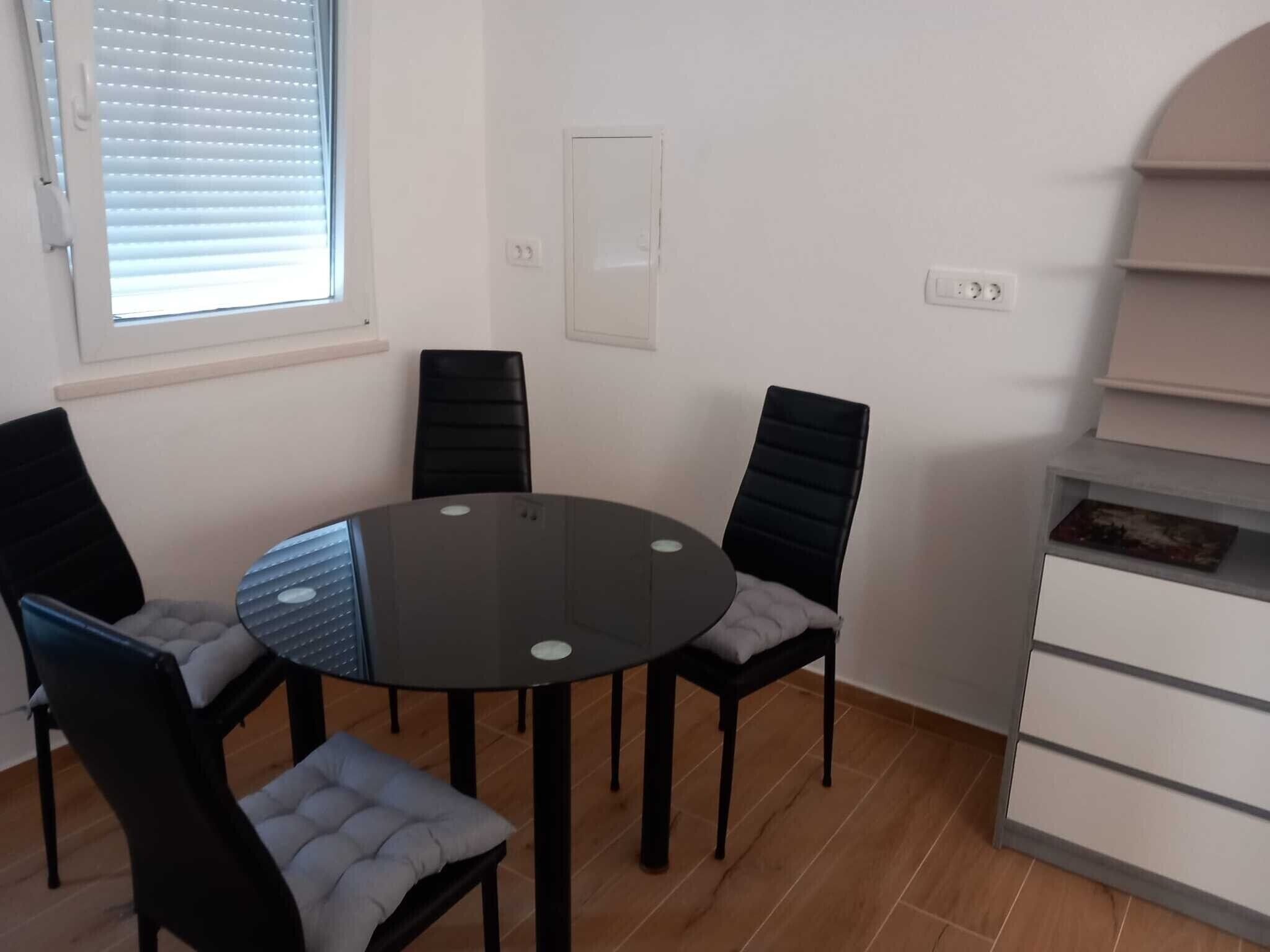 Ein runder Tisch mit vier Stühlen, ein Fenster mit Jalousien und ein weißer Schrank mit Schubladen.