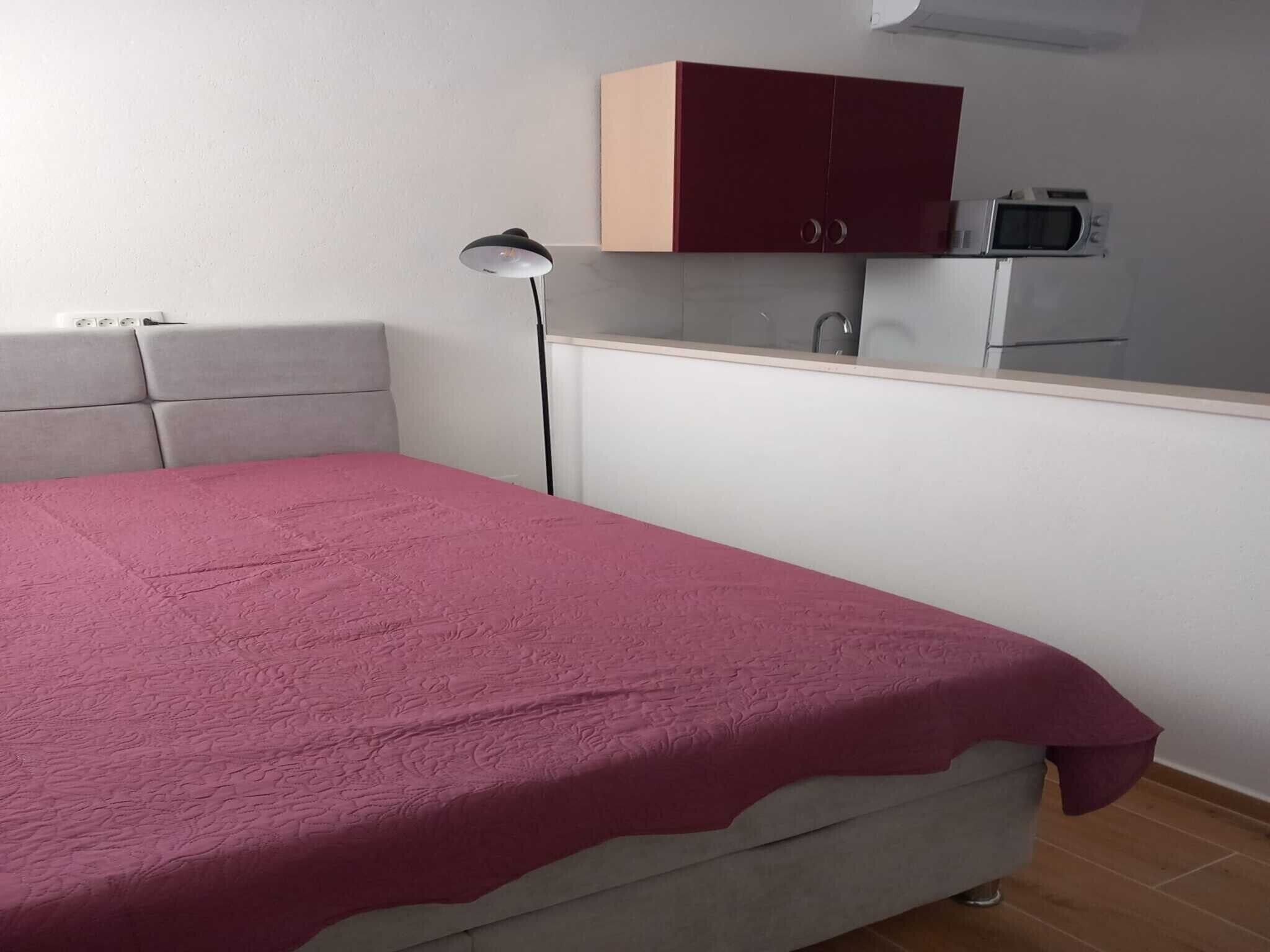 A bedroom with a bed, a nightstand, a desk, a cabinet, and a microwave.