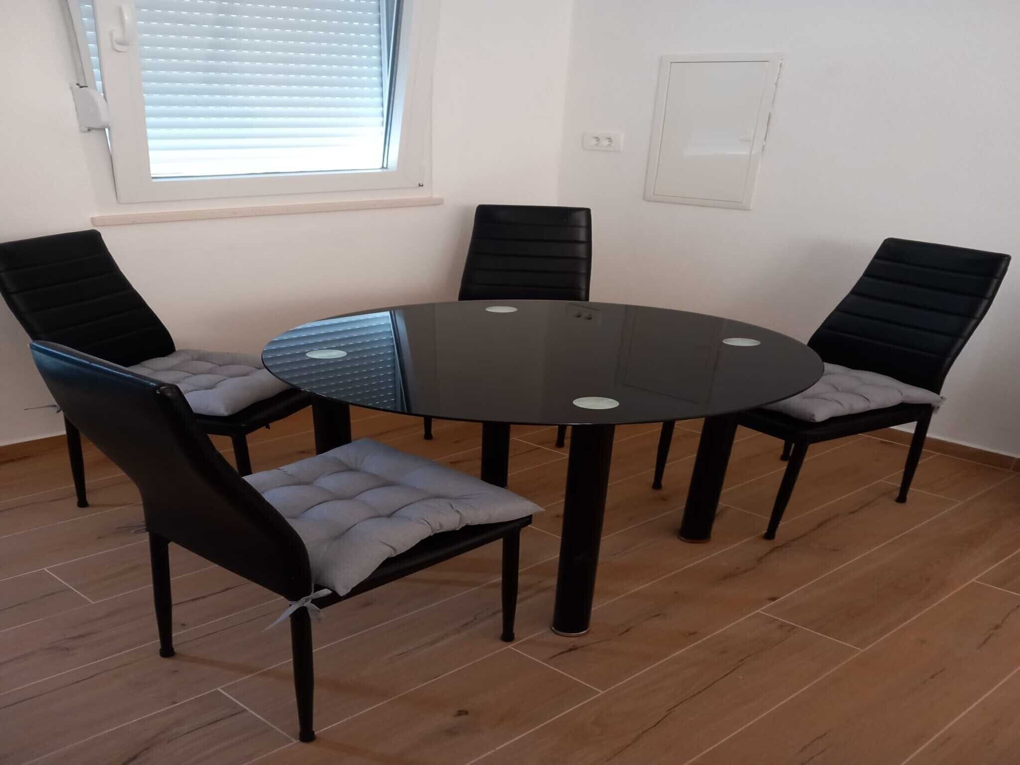 A room with a round glass table surrounded by four black chairs with grey cushions.