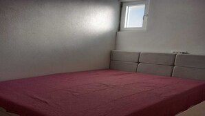 A small, single-bed room with a plain wall, a window, and a red bedspread.