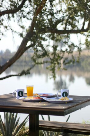 Ein Holztisch mit Frühstücksleckereien und Starbucks-Tassen, mit Blick auf einen stillen See.