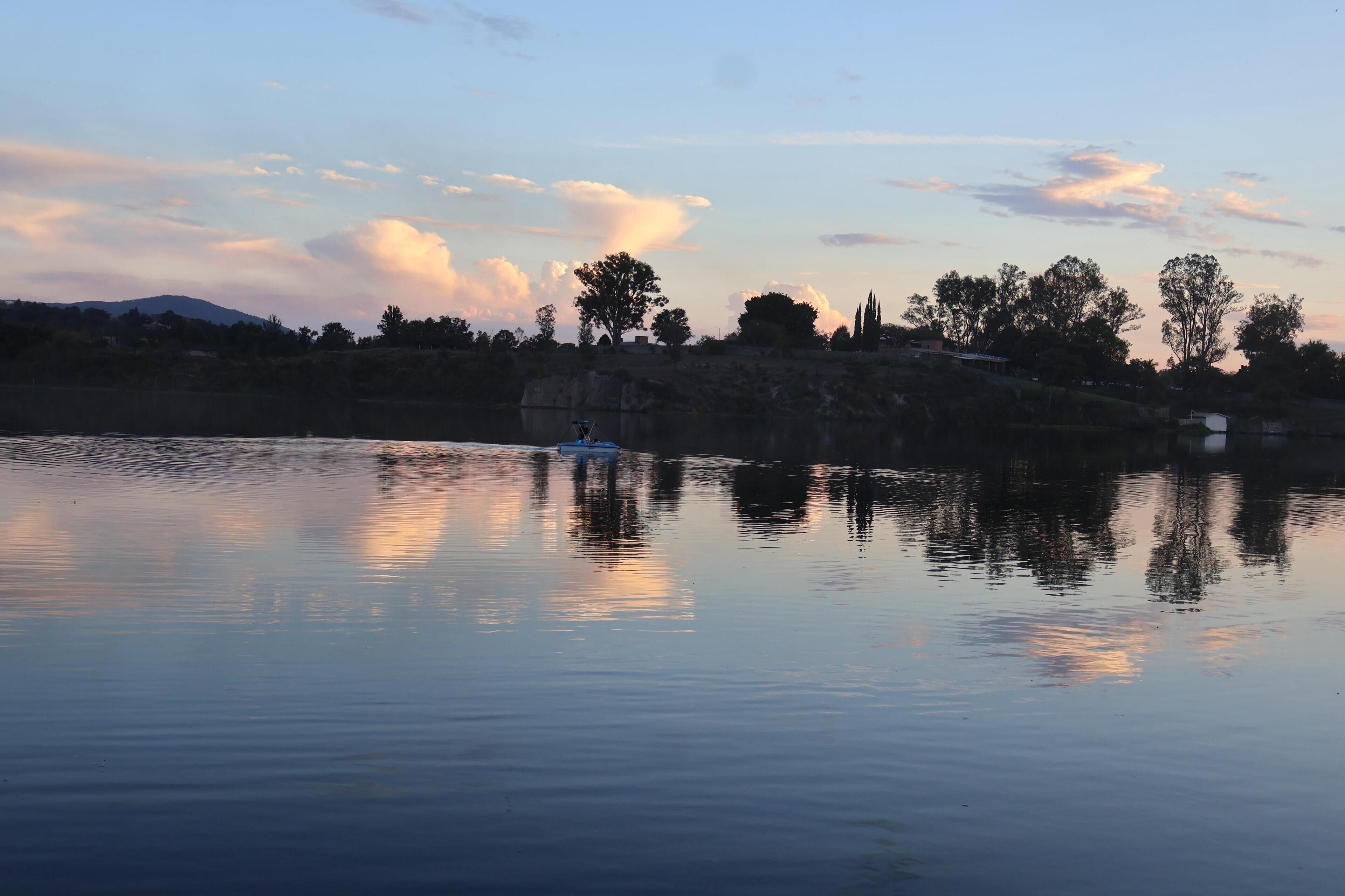 Un lago tranquilo con un bote y una orilla rocosa con árboles.