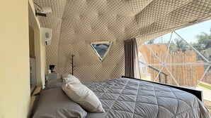 Un dormitorio con un diseño geométrico único en el techo, una cama con colcha gris y una ventana pequeña.