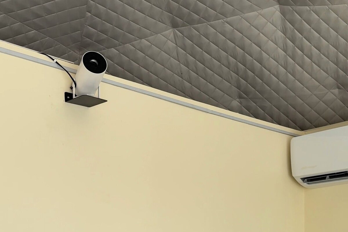 A room with a bed, a pillow, a pair of shoes, a wall-mounted air conditioner, and a ceiling with a quilted pattern.
