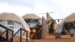 Dos personas sentadas en una manta junto a una piscina, con tiendas de campaña modernas al fondo.
