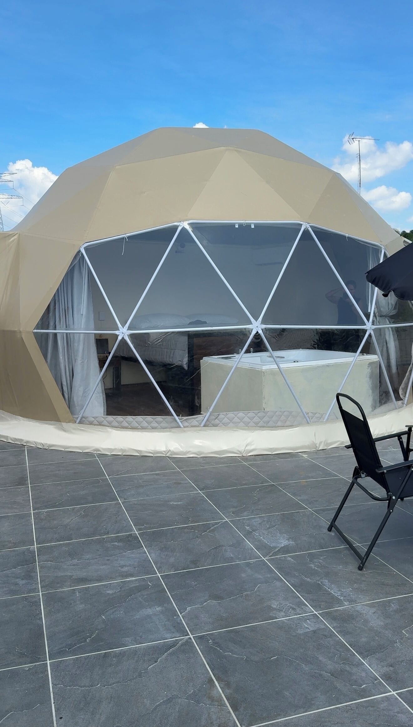 Una struttura a cupola geodetica con tetto trasparente, una piccola area chiusa con una panchina e un pavimento piastrellato.