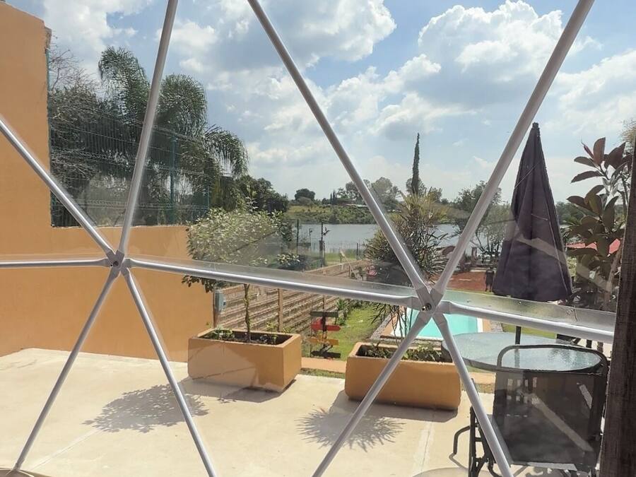 Un espacio al aire libre cubierto con una estructura metálica geométrica, piscina y mobiliario exterior.