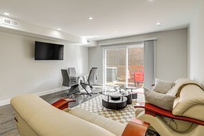 A modern living room with a sofa, coffee table, and chairs. There is a TV mounted on the wall and a balcony with a red chair.