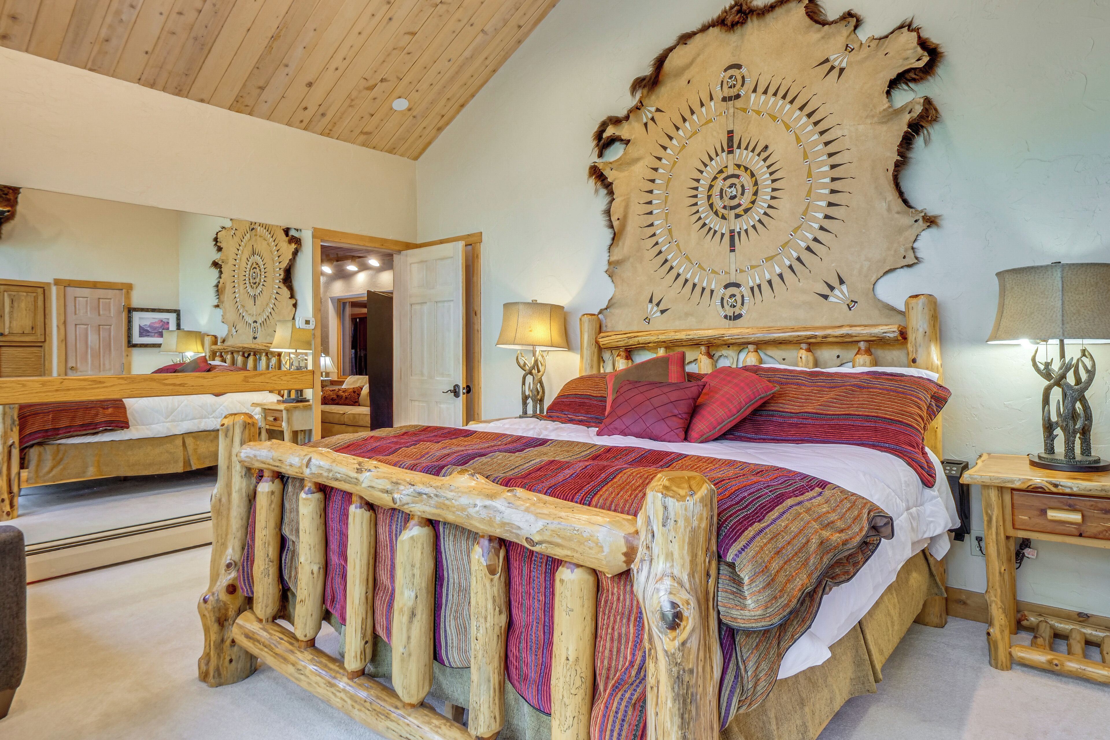 Une chambre à coucher au style rustique, avec un grand lit doté d’une tête de lit en bois, une commode en bois et un miroir.