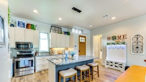 Una cucina moderna con pensili bianchi, un'isola centrale con sgabelli, elettrodomestici in acciaio inossidabile e un'insegna con la scritta 'HOME' al muro.