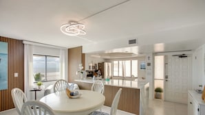 Una cocina moderna con armarios blancos, una isla central y un comedor con una mesa redonda y sillas blancas.