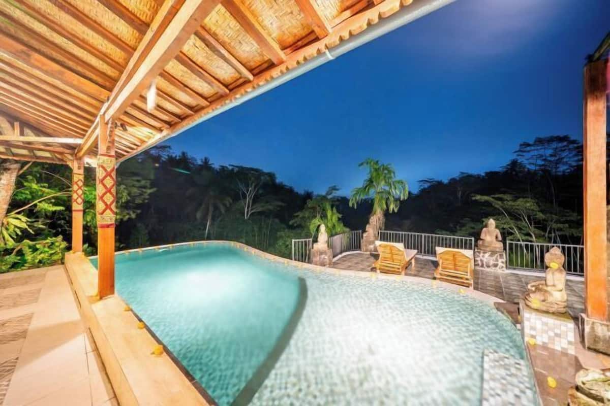 A swimming pool with a wooden deck, a covered seating area, and a statue.