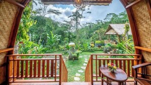 A wooden deck with a view of a lush garden and a thatched-roof structure. - Yoga Maya Villa (Bali)