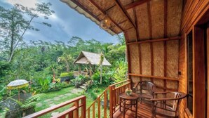 A wooden deck with chairs, a small table, and a thatched-roof structure in a lush garden. - Yoga Maya Villa (Bali)