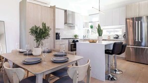 Et moderne køkken med en central ø, rustfrie stålapparater og et spiseområde med et bord dækket til fire personer.