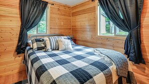 Dormitorio de cabaña de madera con cama, cortinas y ventana.