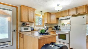 Una cocina con armarios de madera, microondas, estufa, refrigerador y una pequeña isla con pileta.