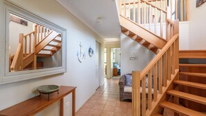 A hallway with a wooden staircase, a mirror, a small table, and a wicker sofa.