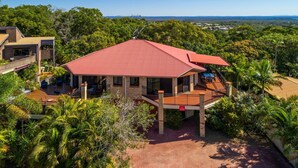 A two-story house with a red roof, surrounded by lush greenery and a clear view of the landscape.