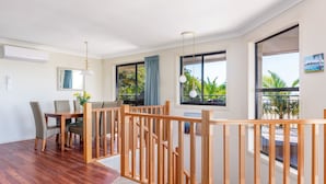 A modern living room with a wooden dining table, chairs, and a balcony with a view of palm trees.