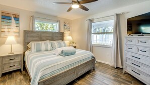 Un dormitorio con cama, mesitas de noche, ventilador de techo, cómoda y televisor.