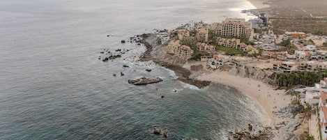 En kystby med bygninger langs stranden, en klippefyldt kystlinje og både i det fjerne.