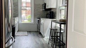 Een moderne keuken met witte kasten, een roestvrijstalen koelkast, een koffiezetapparaat en een raam voor natuurlijk licht.