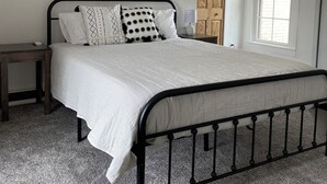 Een slaapkamer met een bed, nachtkastje, wandtapijt, houten deur en een raam.