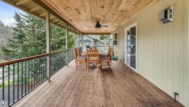 A wooden deck with a table and chairs, a ceiling fan, and a view of trees and houses.