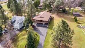 An aerial view of a residential area with a large two-story house featuring a covered porch, surrounded by trees and a well-maintained lawn.