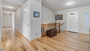 A spacious hallway with wooden flooring, white walls, and a staircase with a wooden railing.