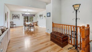 A spacious living room with a wooden floor, a dining area with a table and chairs, and a staircase with a decorative lamp.