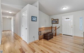 Un hall d’entrée spacieux, doté d’un parquet, de murs blancs et d’un escalier avec une rampe en bois.
