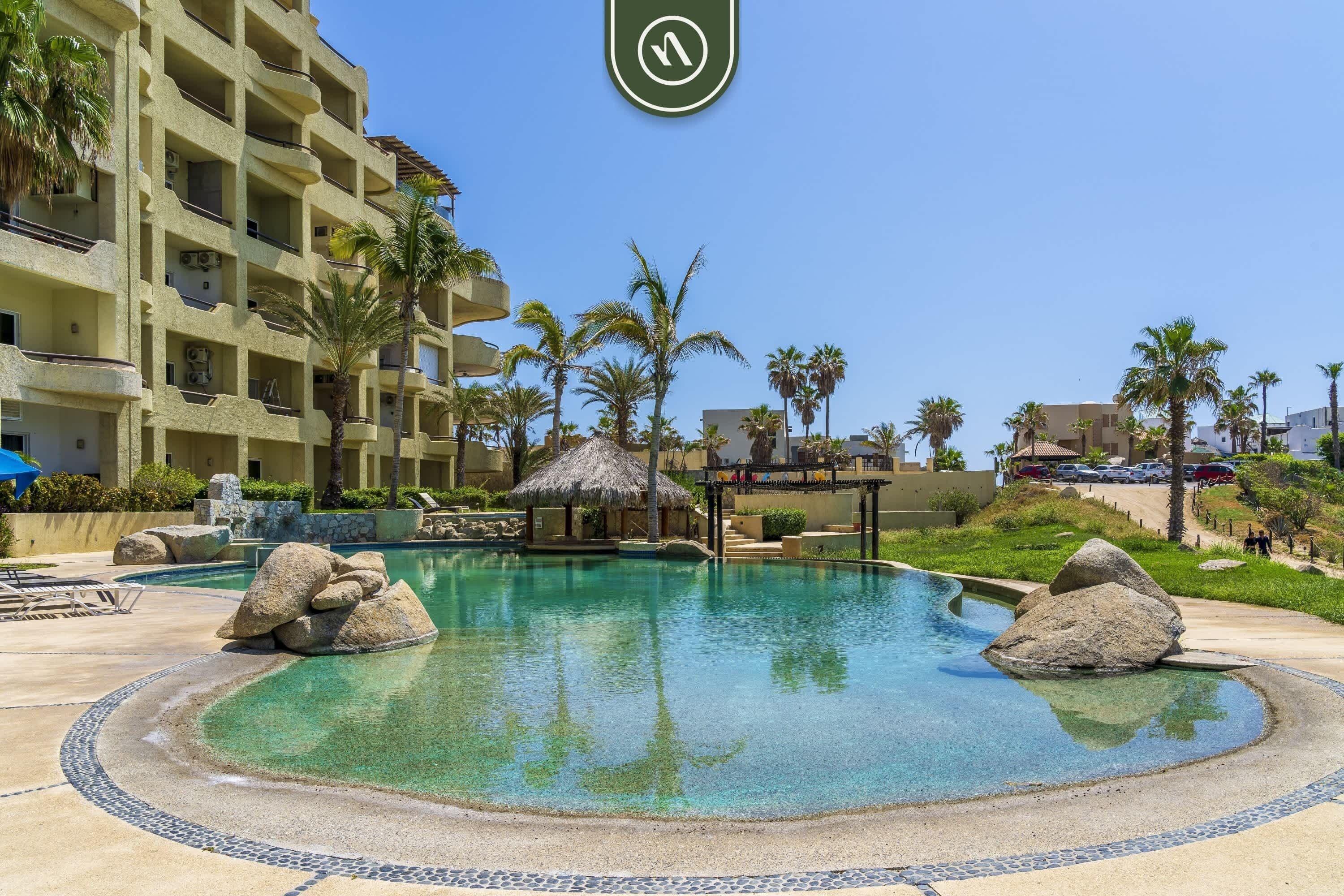Piscina de resort con agua cristalina, rodeada de palmeras y un edificio con balcones.