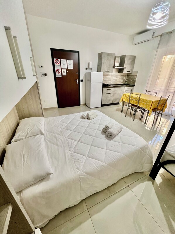 A hotel room with a bed, a small kitchenette, and a dining area.