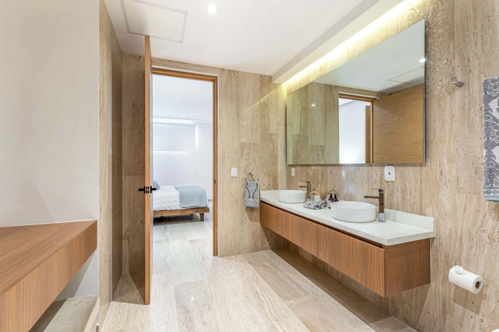 A modern bathroom with two sinks, a large mirror, and a wooden vanity.