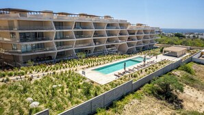 A modern hotel with a pool, outdoor seating, and a view of the sea. - Luxury 2 BR Condo - Oceanview Pool - Gym (Cabo San Lucas)