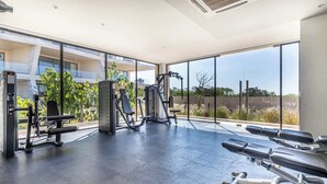 A gym with exercise equipment, large windows, and a view of greenery. - Luxury 2 BR Condo - Oceanview Pool - Gym (Cabo San Lucas)