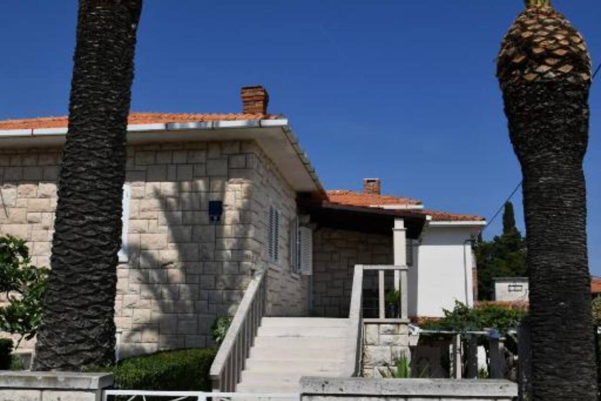 A stone building with a tiled roof, a staircase, and palm trees.
