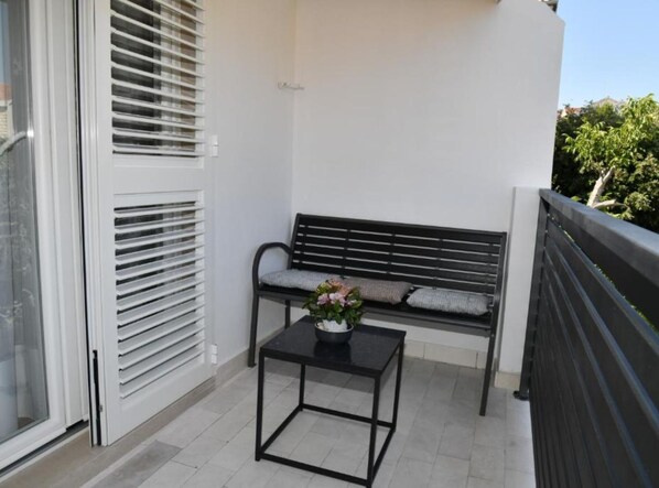 A balcony with a black metal bench, a small table with a vase of flowers, and a white door with blinds. - Apartments Near Sea Supetar (Supetar)