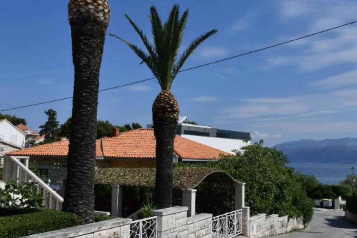 A coastal property with a red-tiled roof, palm trees, and a view of the sea.