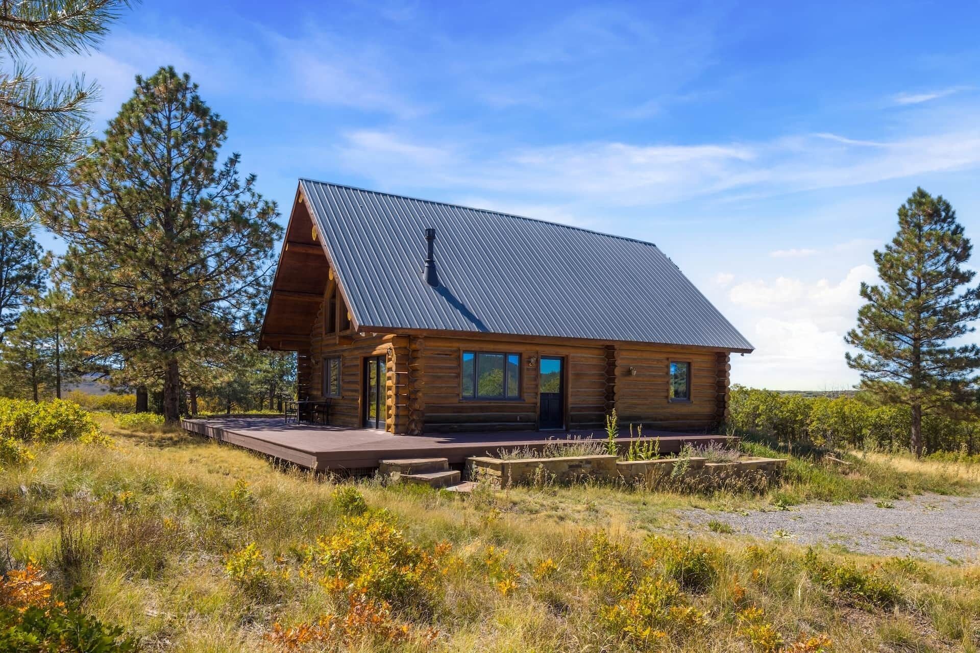 Eine Blockhütte mit Metallbedachung, einer Holzdachterrasse und von Bäumen und Gras umgeben.