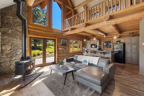 A log cabin interior with a stone wall, a fireplace, a sofa, and a kitchen area. - Mesa Vista: 3 bed/2bath Mountain Retreat (San Miguel County)