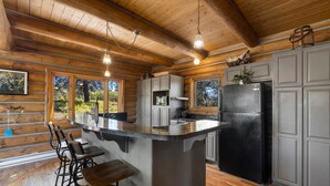 Cocina de cabaña rústica con una isla central, taburetes de bar, un refrigerador y piso de madera.