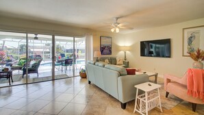 A living room with a sofa, a coffee table, and a TV. There is a balcony with chairs and a table. - Hot Tub + Heated Pool, Gulf Access, Waterfront with Lanai TV (Cape Coral)