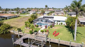 A residential property with a swimming pool, a dock, and a well-maintained lawn. - Hot Tub + Heated Pool, Gulf Access, Waterfront with Lanai TV (Cape Coral)