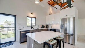 Een moderne keuken met een groot kookeiland, roestvrijstalen apparatuur en uitzicht naar buiten.