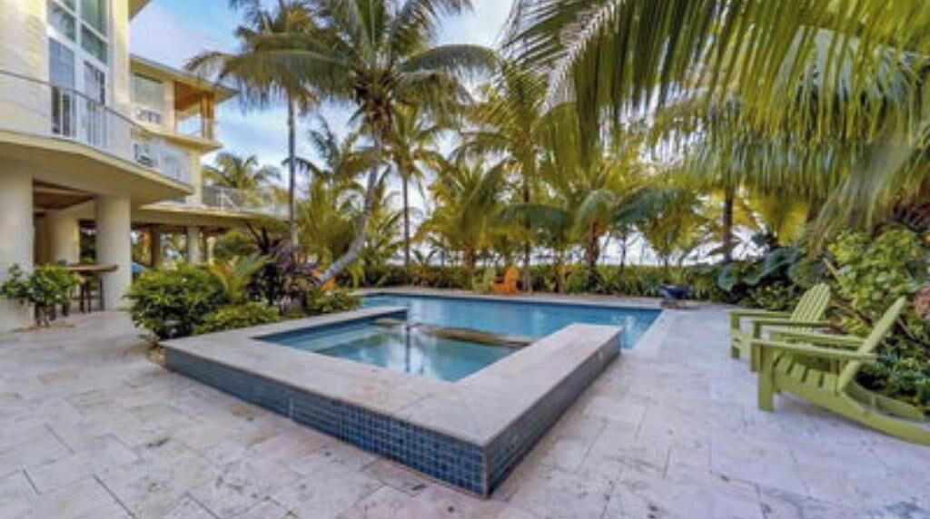 A pool area with a rectangular pool, surrounded by palm trees and greenery, and a building with balconies.