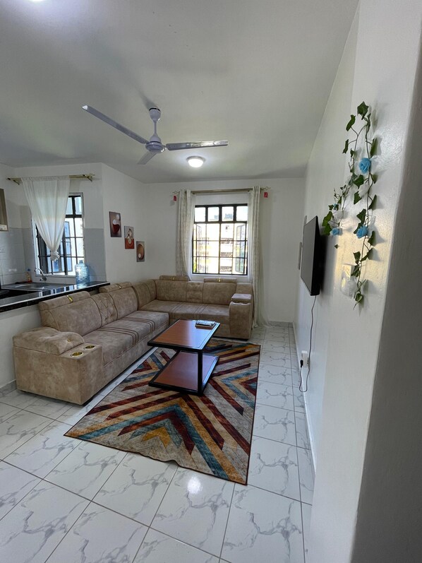 A living room with a sofa, a coffee table, a TV, and a ceiling fan.